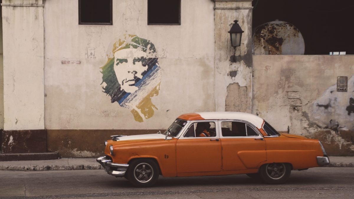 Vintage GAZ-21 car in Havana against a mural background, capturing Cuban street life.